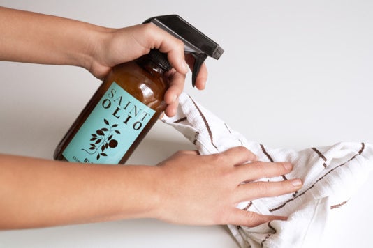 Person spraying Saint Olio on a piece of cloth.